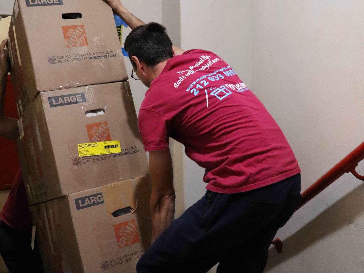 Movers carrying a stack of boxes up the stairs of a NYC walk-up apartment building