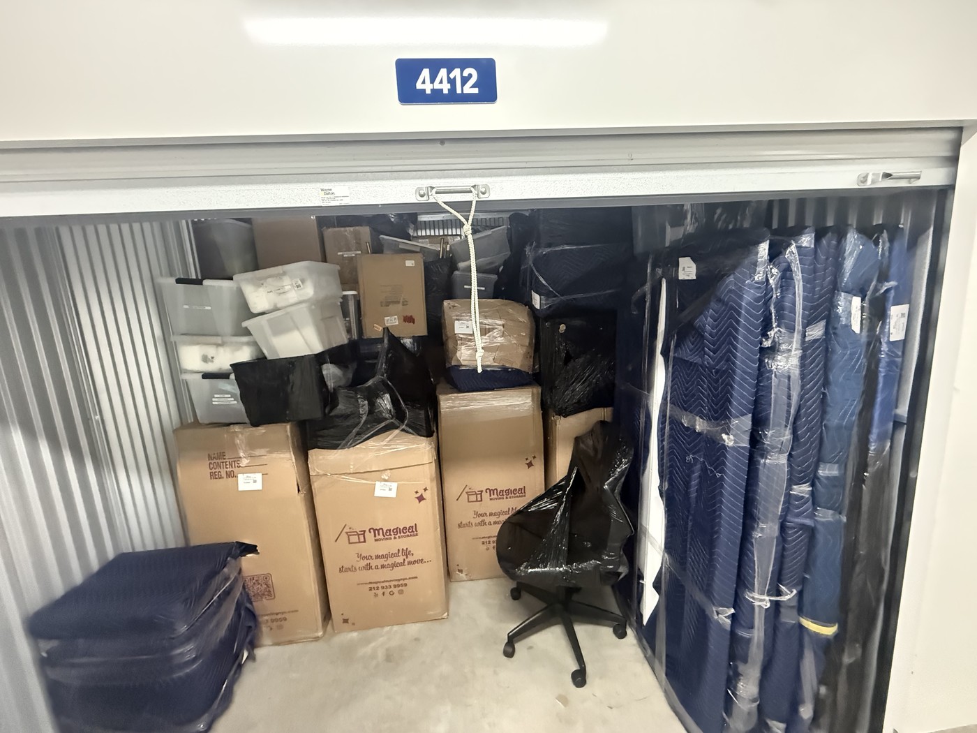 Storage unit with boxes and wrapped furniture, where the second couch goes when moving in together
