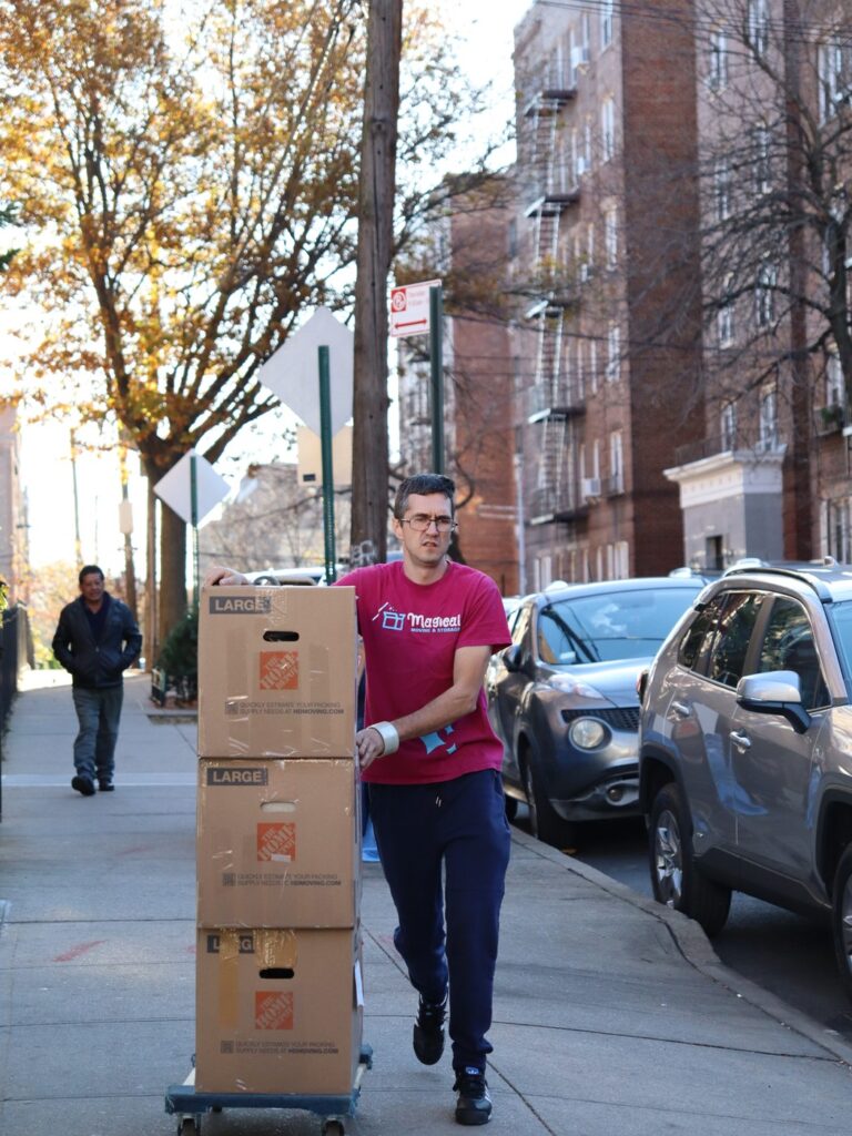 Mover pushing a hand truck of boxes down a New York sidewalk, moving on NYC Marathon Sunday