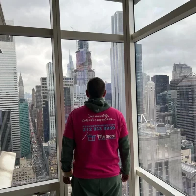 A mover standing in front of a window looking down on the NYC streets, with Magical Moving & Storage printed on the hoodie