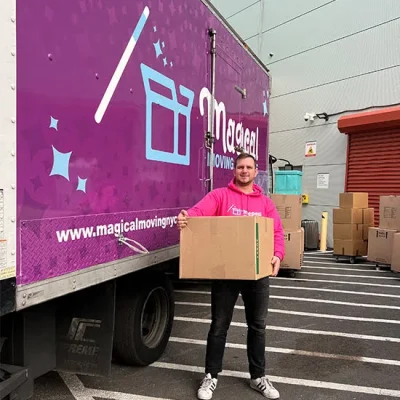 A mover standing in front of a pink moving truck next to their storage