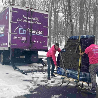 Two movers loading a piano into their truck during winter