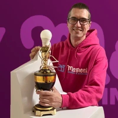 Mover in pink hoodie packing a lamp in front of Magical Moving & Storage wrap