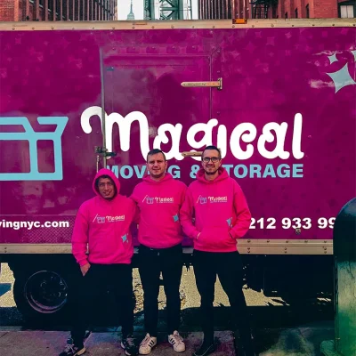 Three movers in NYC standing in front of a pink truck, smiling at the camera